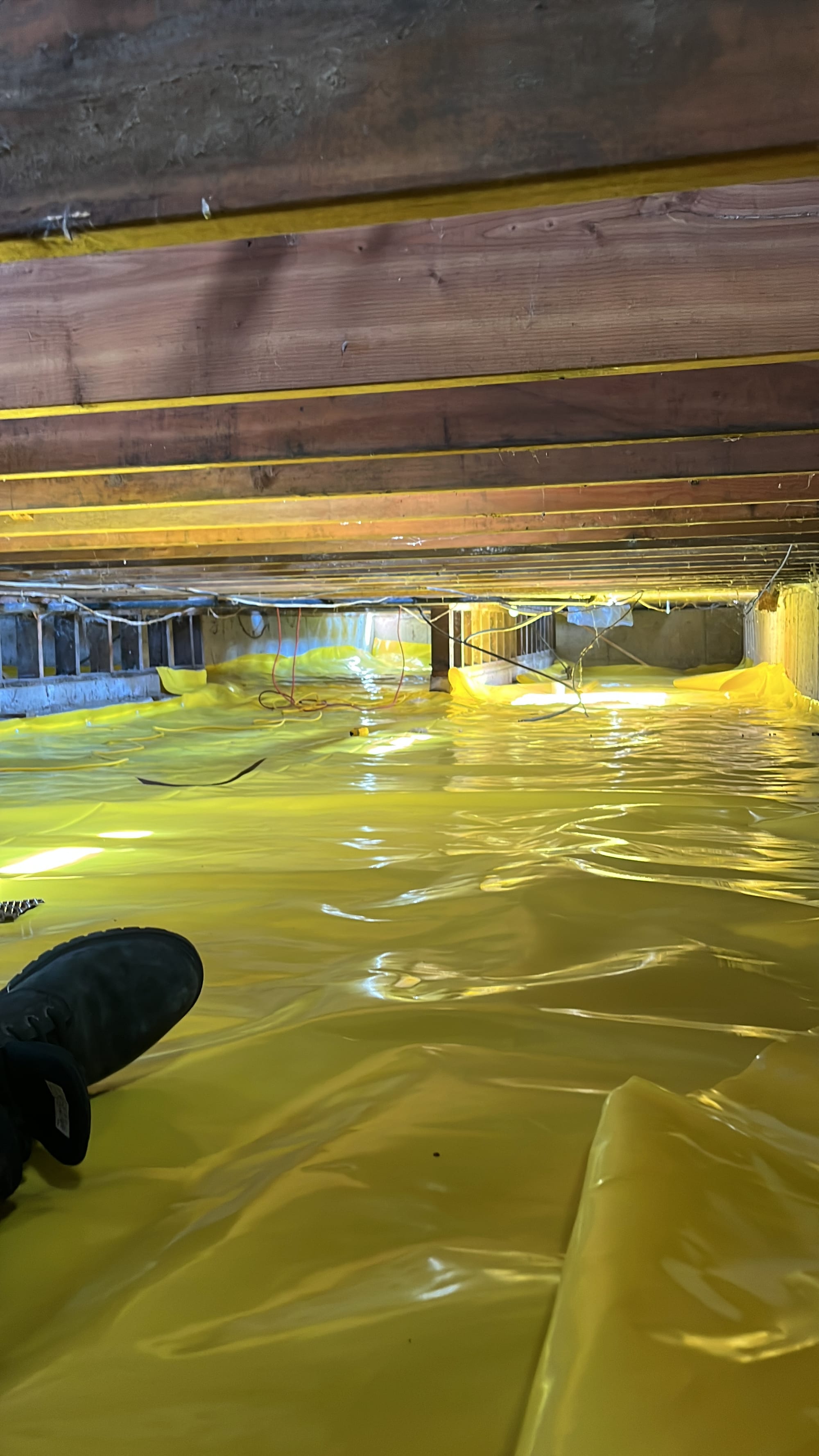 Completed crawlspace encapsulation — sealed yellow vapor barrier on floor and walls