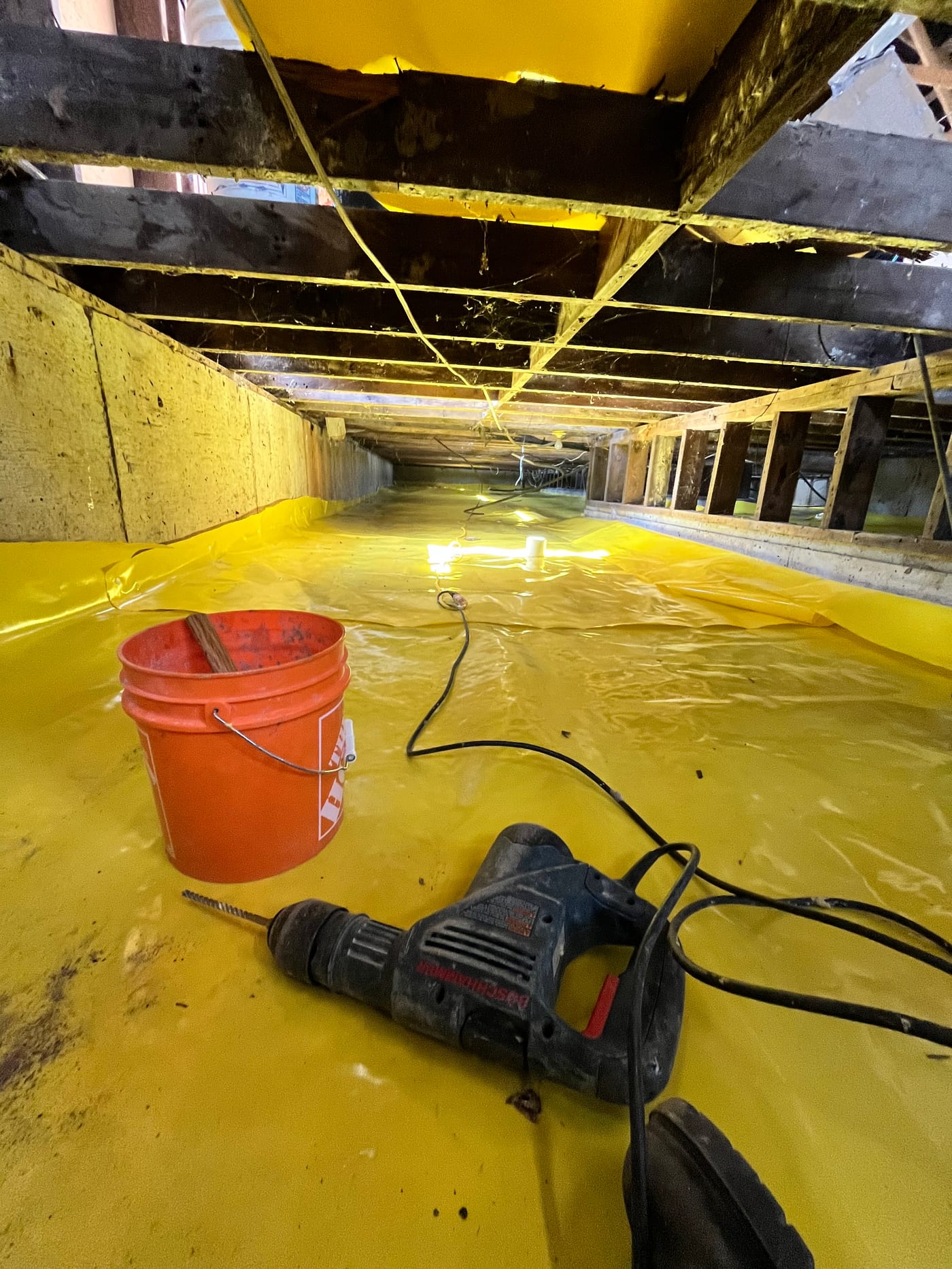 Active crawlspace encapsulation in progress with hammer drill and yellow vapor barrier